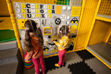 Fototapeta premium Two sisters playing with busy board at kids play center.
