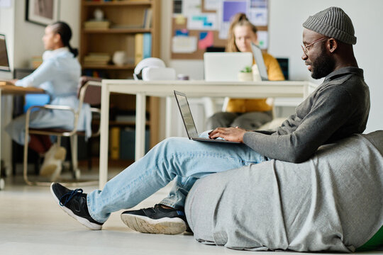 African American man sitting on comfortable bag chair and working online on laptop in office