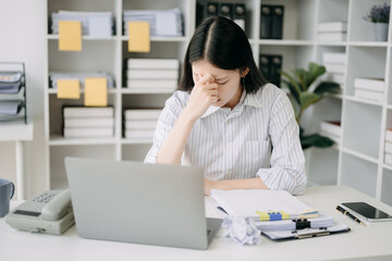 Asian business woman is stressed, bored, and overthinking from working on a tablet at the modern office.