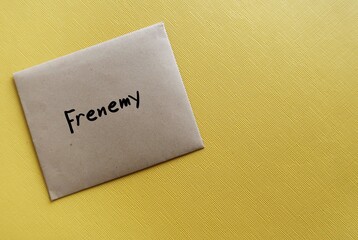 Envelope on copy space yellow background with text written FRENEMY - person who combines the characteristics of friend and enemy, rival pretends to be a friend