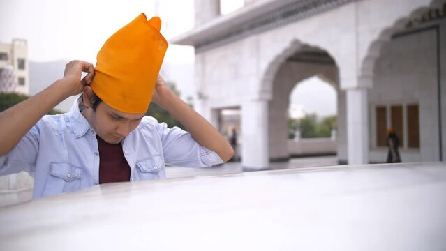 Rajasthan  Pushkar  India  A boy wearing an orange head scarf before praying at a Gurdwara - a Sikh religion  rituals. A handsome man in casual clothes is worshipping the Almighty - religious faith...