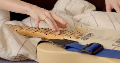 Women's hand ring finger touches the strings of the guitar on the bed. Relaxed state of the body, mental recovery, tactile contact of the string. Pleasant feeling in the fingers.