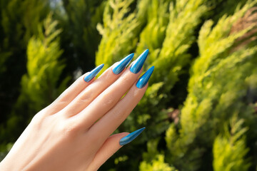 Female hand with summer nail design. Glitter blue nail polish manicure. Female hand on tropical background.