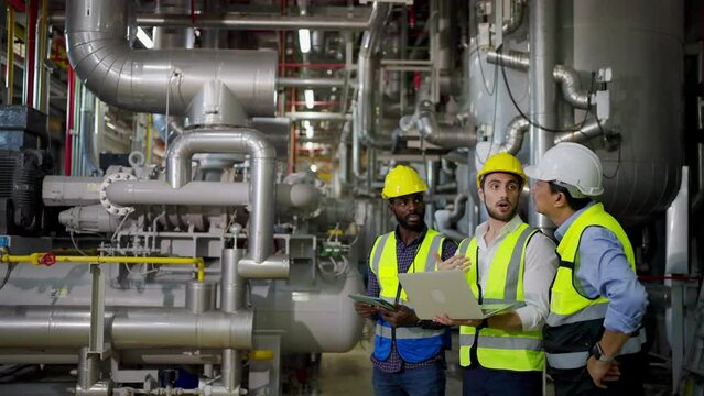 Group of Diversity electrical engineer in safety uniform working together at factory site control room. Industrial technician worker maintenance and checking power system at manufacturing plant room.