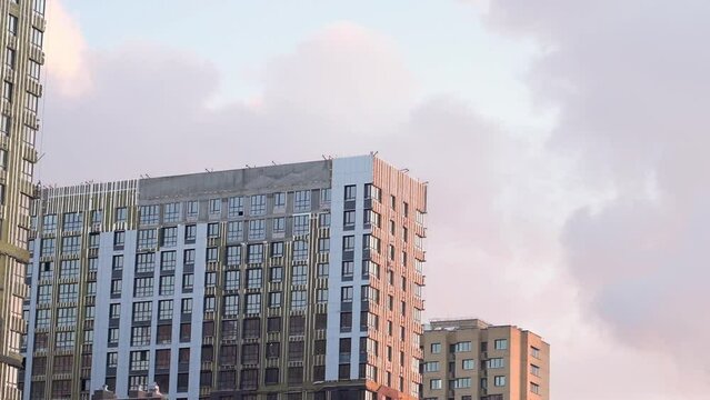 Installation of external thermal insulation of walls with stone wool on Monolithic concrete frame of an apartment building under construction with partially attached facade cladding blocks with clouds