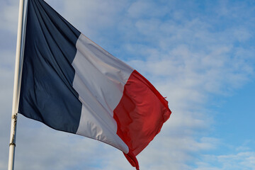 Straight on view of a waving French flag against a bright blue sky.