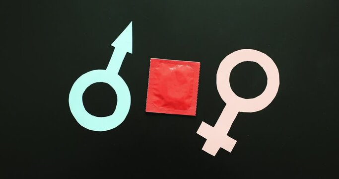 Female hand puts condom pack on male and female symbols on black background. Protection from sexually transmitted diseases. Prevention of unwanted pregnancy
