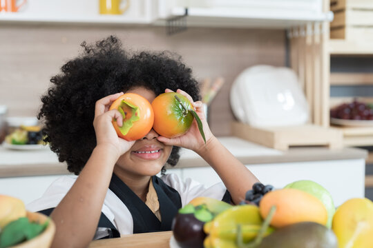 Happy child girl holding and playing orange in the kitchen. Smiling child girl with fruit in the kitchen