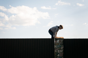A little boy climbs over the fence