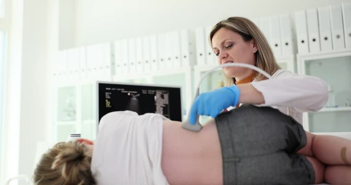 Positive female doctor checks little girl kidneys using modern ultrasound equipment with transducer probe. Medic looks at screen to examine sick organs