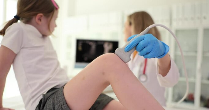 Young female doctor checks sore knee of little girl using ultrasound equipment. Pediatrician conducts research with transducer probe to determine cause of patient pain