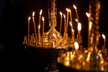 Church candles are burning on a large golden candlestick in the orthodox church. burning candles in the orthodox church. Christian faith and traditions. Theme of faith and God, religion and traditions