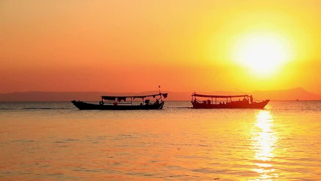 Dreamy summer scene of two traditional khmer long boat silhouette crossing paths on the sunset horizon in Koh Tonsay or Rabbit Island in Cambodia