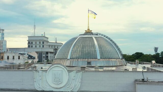 Top part of white parliament building called Verkhovna Rada in Kyiv. Coat of arms and waving flag of Ukraine.