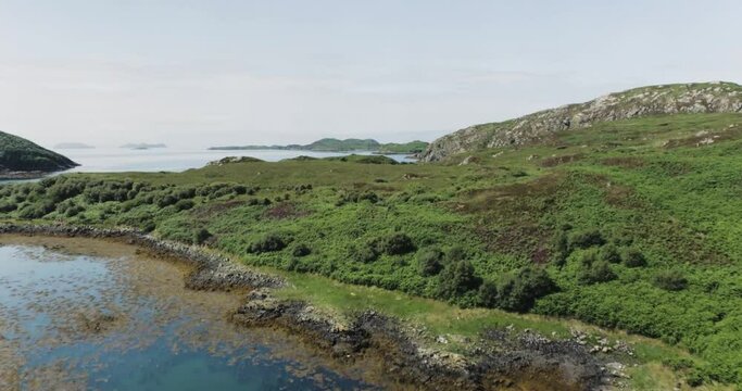 Slow push in drone shot showing the terrain along scotland coastline looking out to sea and the Hebrides
