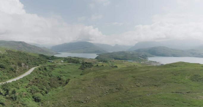 Dramatic drone shot of the scottish coastal highlands with cloudy blue skies and coastal road