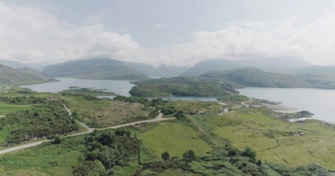 Dramatic drone pull showing the scottish coastal highlands with cloudy blue skies, mountain terrain and coastal road