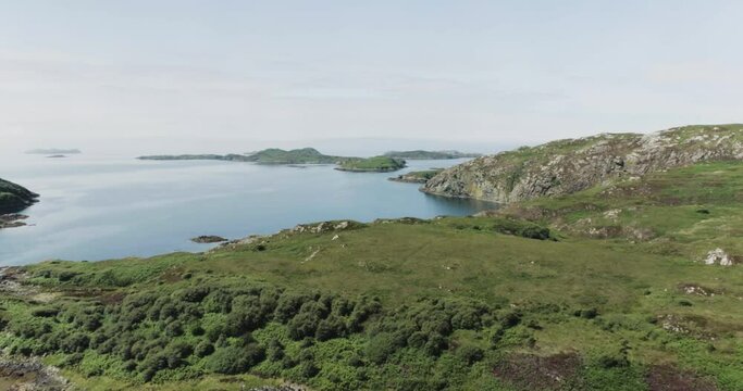 Slow pull back drone shot showing the coastline terrain in scotland looking out to sea and the Hebrides
