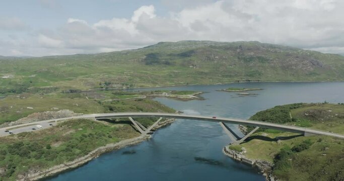 Wide drone shot of moving traffic over the Kylesku Bridge along scotland northcoast 500 route showing the mountain and sea terrain