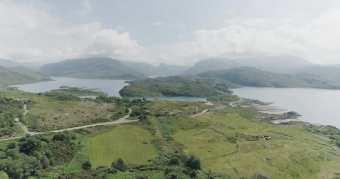 Dramatic drone pan of the scottish coastal highlands with cloudy blue skies, mountain terrain and coastal road