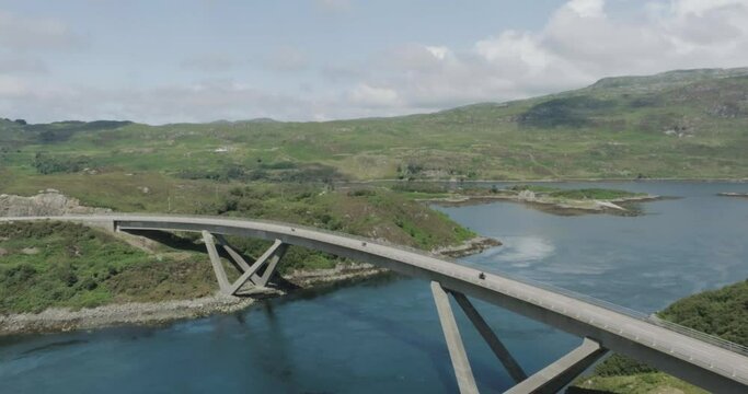 Pull back drone shot of a three motorbikes in convoy over Kylesku Bridge along scotland northcoast 500 route