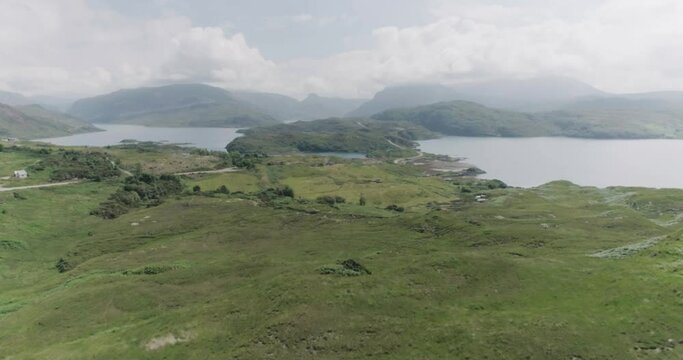 Dramatic drone push in of the scottish coastal highlands with cloudy blue skies, mountain terrain and coastal road