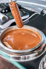Salesman wearing plastic gloves dips ice cream on stick into hot chocolate. Process of popsicle making on special counter in city resort