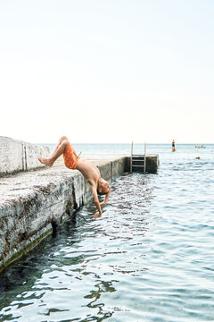 Junior schoolboy unsuccessfully performed back-flip from pier into azure sea. Boy falls into sea water doing wrong jump from beach