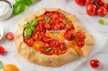 Tomatoes galette or pie with cheese and herbs on a white wooden background. Vegetarian dish. Selective focus.