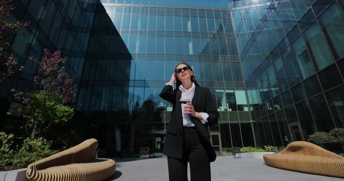 Businesswoman in sunglasses outdoors, drinking coffee to go. Woman entrepreneur in a formal suit drinking coffee to go during a break.