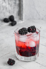 Blackberry Cocktail Gin and Tonic with fresh berries, ice and mint. Refreshing lemonade with blackberry and ice on a tile grey background. Drink photography