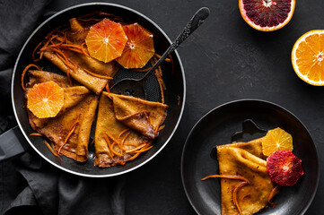 Traditional French Crêpes suzette pancakes with orange sauce in a pan and on a plate on a black...