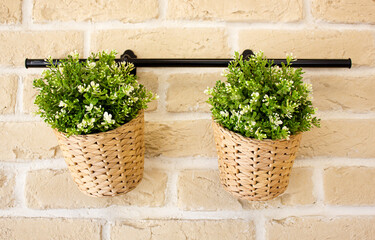 Two artificial flowers in wicker baskets on the background of a brick wall. Decorations, decoration for a room, premises, building, institution.