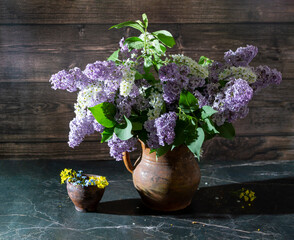 Still life with lilacs and white bird cherry in an old clay vase on a dark marble table. Concept aroma of life.