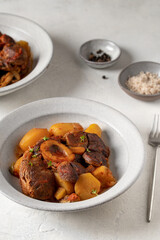 Stew veal shank meat Ossobuco. Traditional Italian Ossobuco alla Milanese served with stew potatoes and vegetables on a white stone background. Horizontal crop