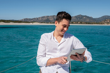Calm male sitting on deck of catamaran and surfing Internet on tablet while enjoying summer vacation