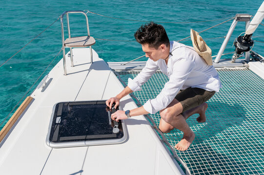 Side view high angle of male opening hatch while sailing on catamaran in sea on sunny day during summer vacation