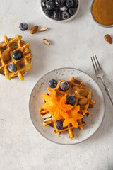 Traditional Belgian waffles with blueberries, persimmon, almond and caramel on white background. Flat lay, top view.