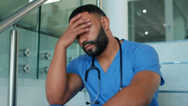 Doctor, man and headache in stress on stairs from burnout, overworked or strain at the hospital. Tired and stressed male medical professional suffering bad head pain, fatigue or mental health anxiety