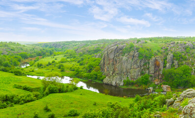 small calm river flow among green hills under cloudy sky