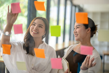 Asian businesswoman sharing opinions and analyzing notes on glass with colleagues in office.