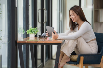 An attractive young Asian female relaxes on her chair in the minimal living room while using a digital tablet.