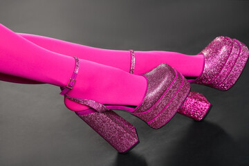 Woman wearing pink tights and high heeled shoes with platform and square toes on dark grey background, closeup