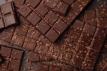 Pieces and shavings of tasty chocolate bars on grey table, flat lay