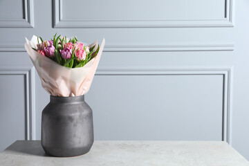 Vase with bouquet of beautiful tulips on grey table. Space for text