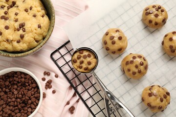 Bowl with dough and uncooked chocolate chip cookies on table, flat lay
