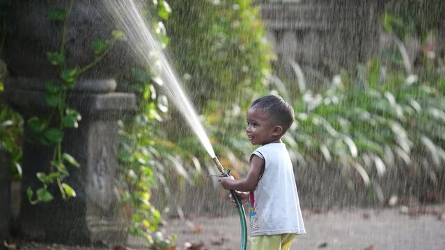 Happy little boy play with water hose. Smile asian child have fun. Cheerful childhood. Laughing kid enjoy rain splash. Joyful wet toddler. Cute baby relax outdoor slow motion. Nice hot day. Cool rest.