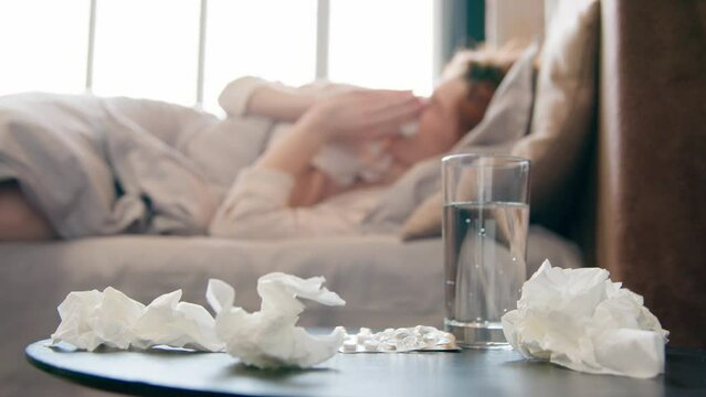 Unhealthy sick ill Caucasian woman sneeze in bed at home bad feeling coronavirus cold flu disease girl suffer headache fever seasonal virus allergy blowing runny nose in tissue napkin health problem