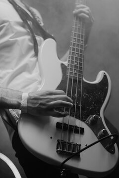 Close-up of bass guitar player in action in the stage fog. Black and white
