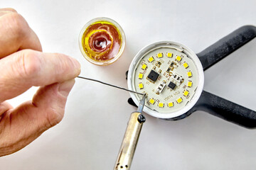 Soldering a burned-out LED into an LED light bulb. Hand with a soldering iron and rosin with solder...
